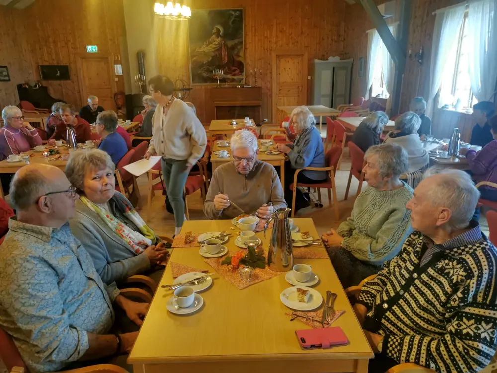 En gruppe eldre mennesker sitter rundt et bord med mat og drikke.