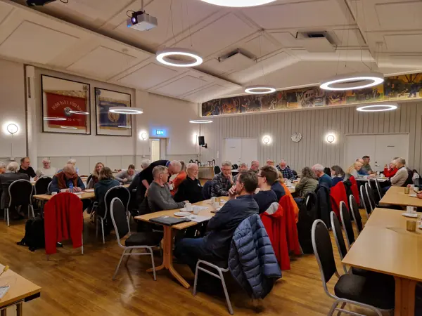 En mengde folk sitter benket rundt langbord i en stor sal