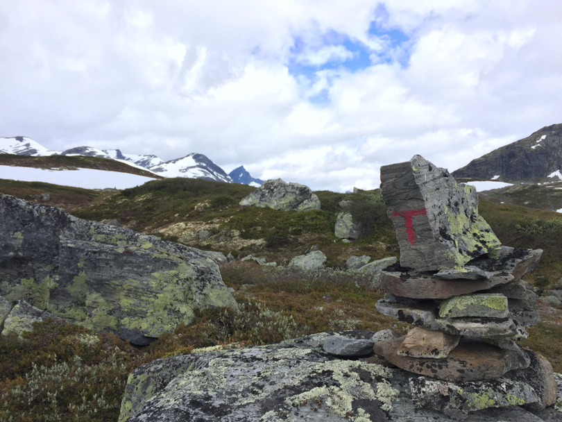 DNT varde med snødekte fjelltopper i bakgrunnen.