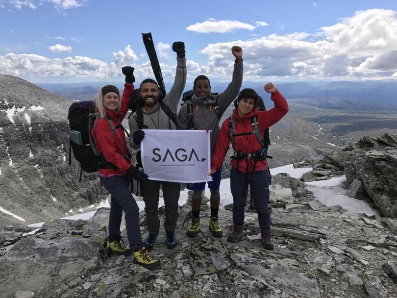 Gruppebilde av de fire ungdommene fra toppen av Rondeslottet. Armene i været og SAGA-plakaten fremme foran den slående utsikten. 