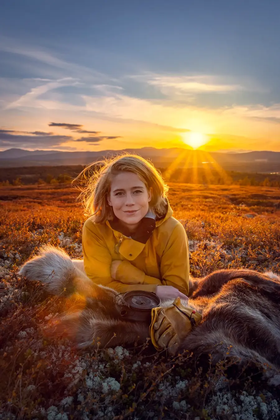 Kvinne ligger på en sovepose med solnedgang i bakgrunn