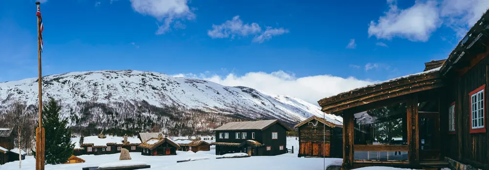 Syv hytter på gårdstunet til Sota Sæter dekket av snø i flott vintervær. 