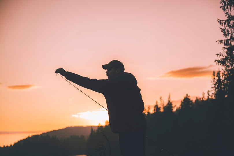 Mann som tar på krok på fiskestang, i solnedgang