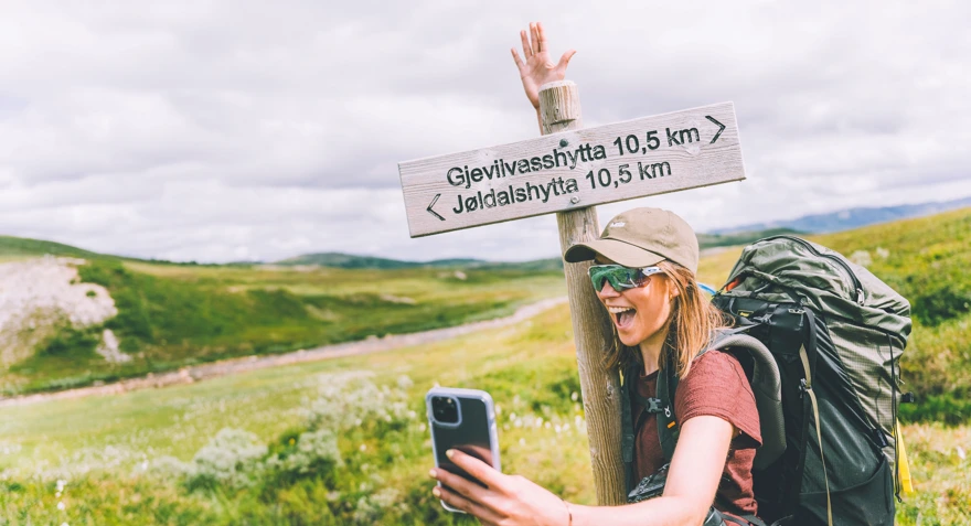 Jente som står og tar en selfie foran en skiltstolpe som viser vei og avstand til Jøldalshytta og Gjevilvasshytta