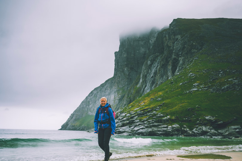 En dame som går på stranden med høyt fjell i bakgrunnen