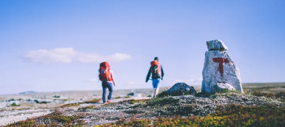 to turgåere går i fjellet, stein med rød t i forgrunnen