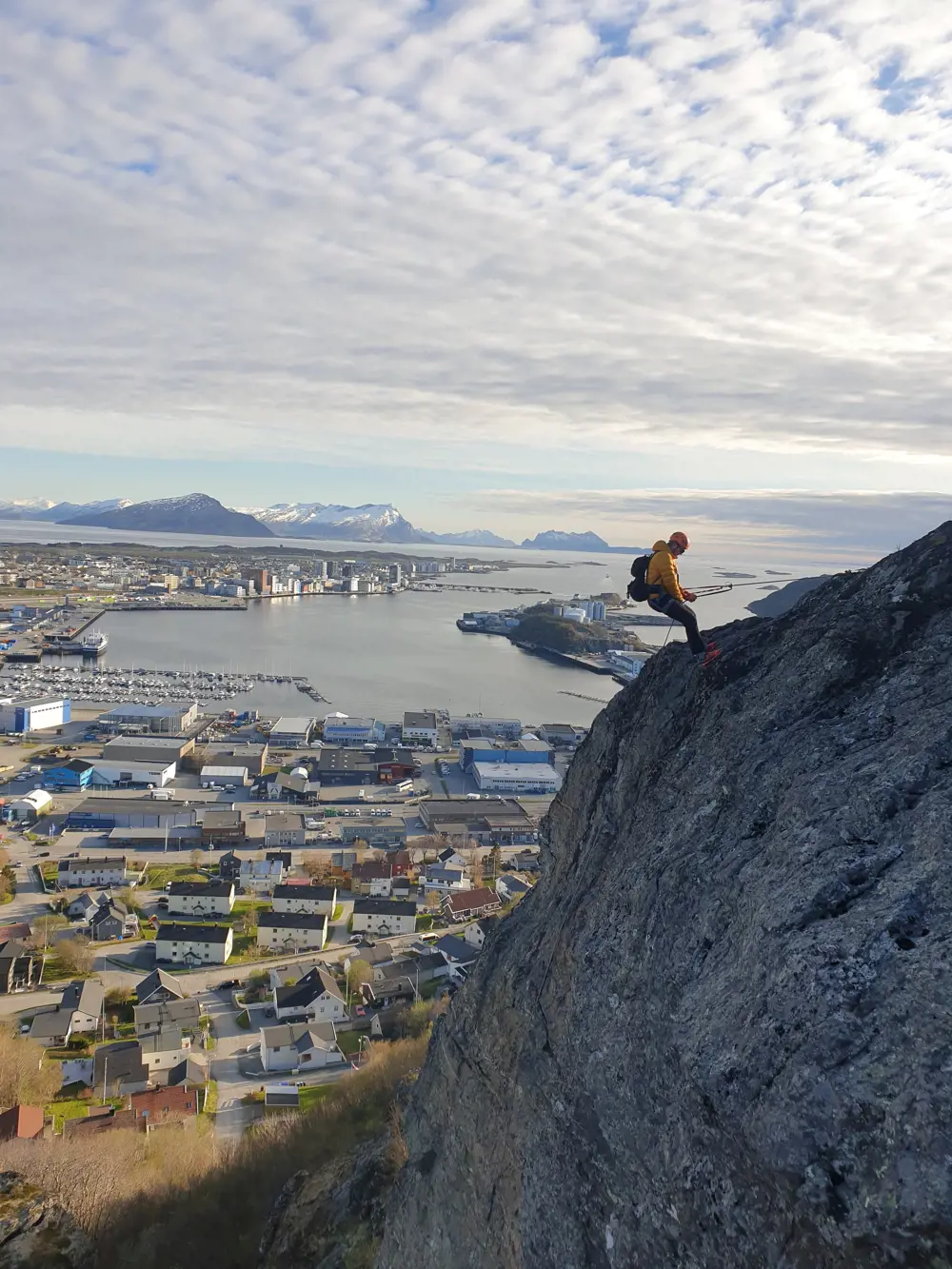 Mann som rapellerer ned fjellet med utsikt til Bodø by