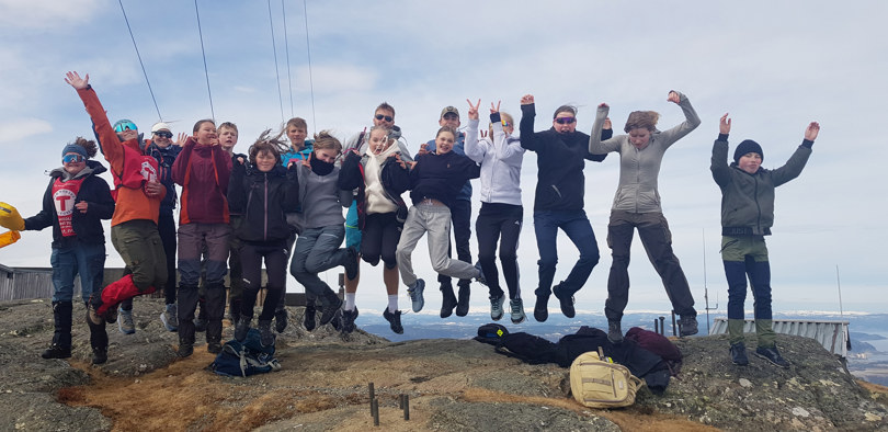 En gjeng ungdommer hopper i lufta samtidig på toppen av et fjell.