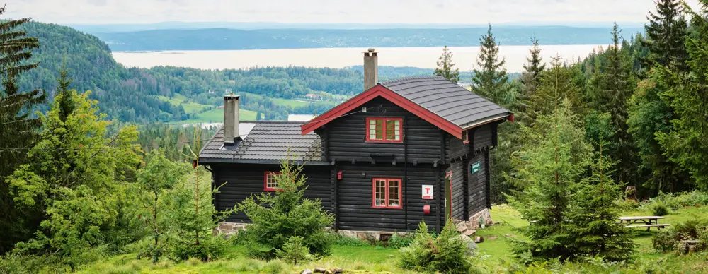 Svartmalt hytte med rødkarmer og fint utsikt mot Oslofjorden i bakgrunnen