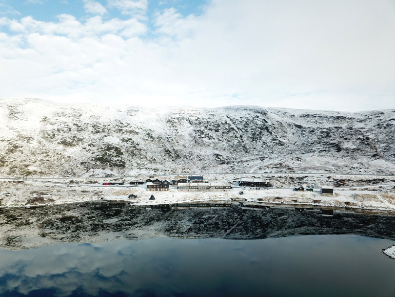 Haukeliseter fjellstue speiler seg i Ståvatn med et melisdryss av snø og en siklar blå himmel