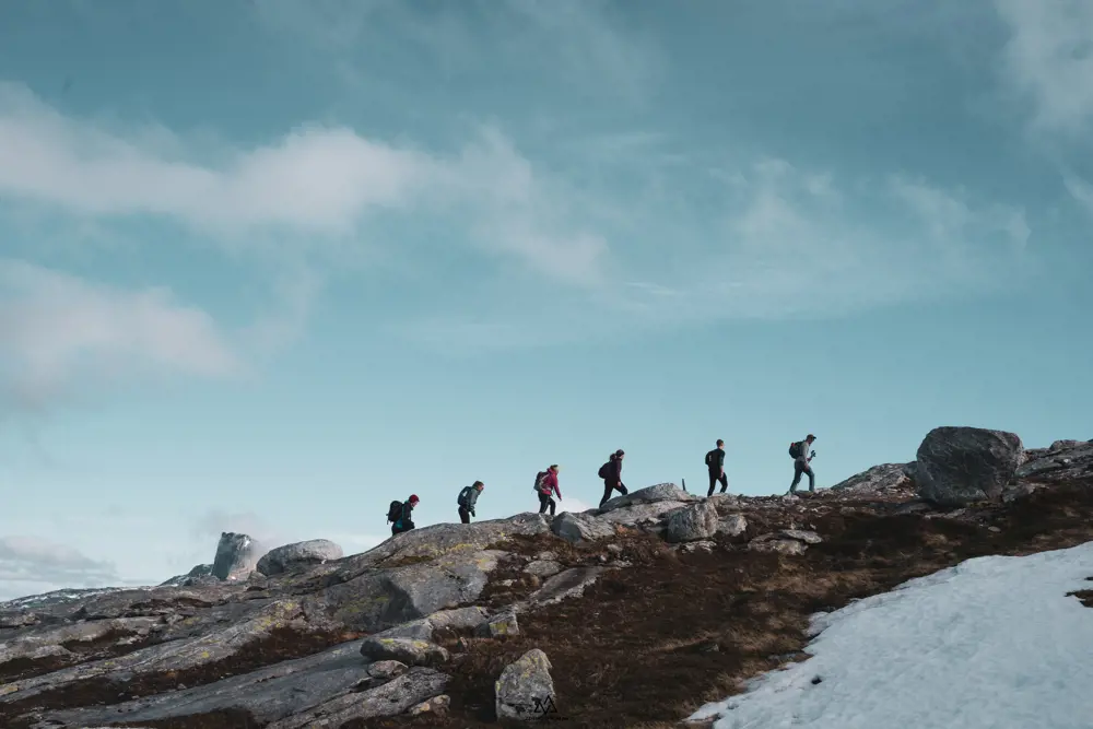 Seks ungdommer vises mot horisonten mens de går oppover ei fjellside