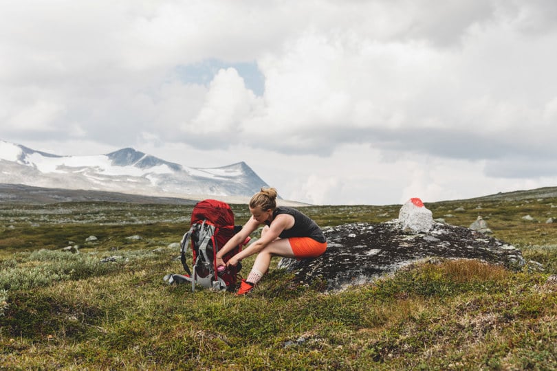 Dame sitter i fjellet, tar noe ut av sekken.