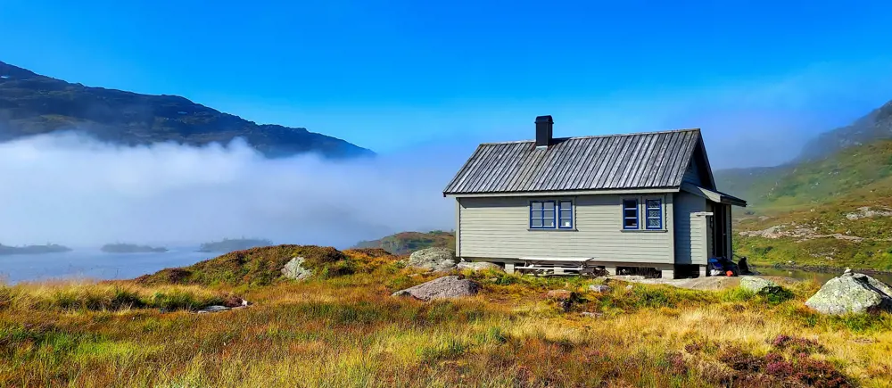 En hytte på fjellet med blå himmel og skodde. Foto.