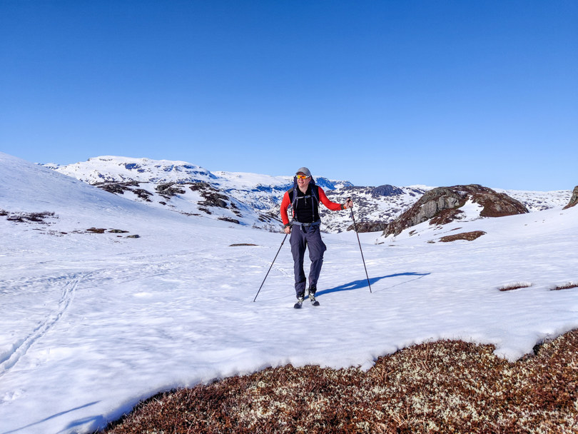 Mann hviler på stavene på skitur i solskinn.