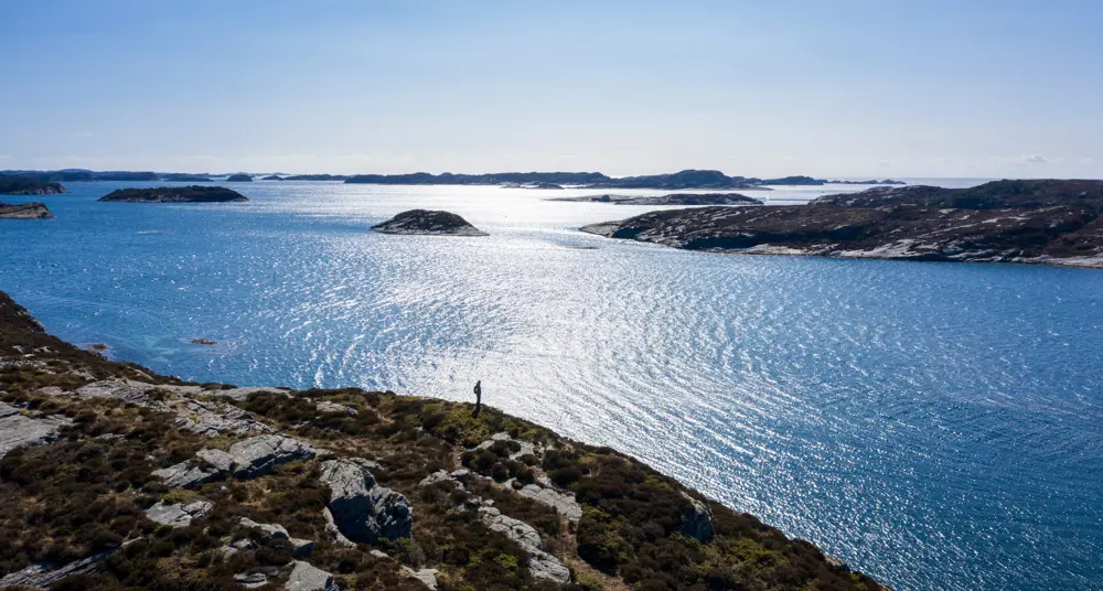 Person på tur langs klipper ute i havgapet. Sol og sjø. Foto