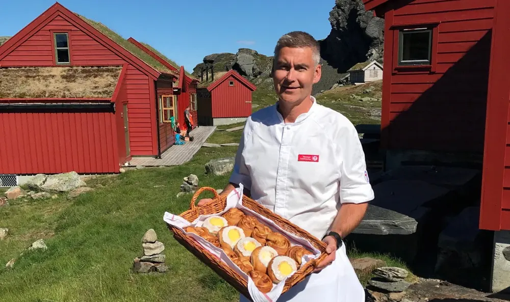 Bilde av bestyreren som holder et fat med skoleboller utenfor hytta.