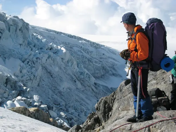 Historisk bilde av mann med ryggsekk og rød jakke som ser utover fjellene.