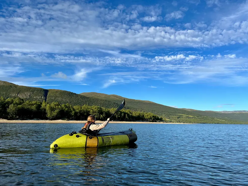 En person i en packraft padler på en innsjø om sommeren