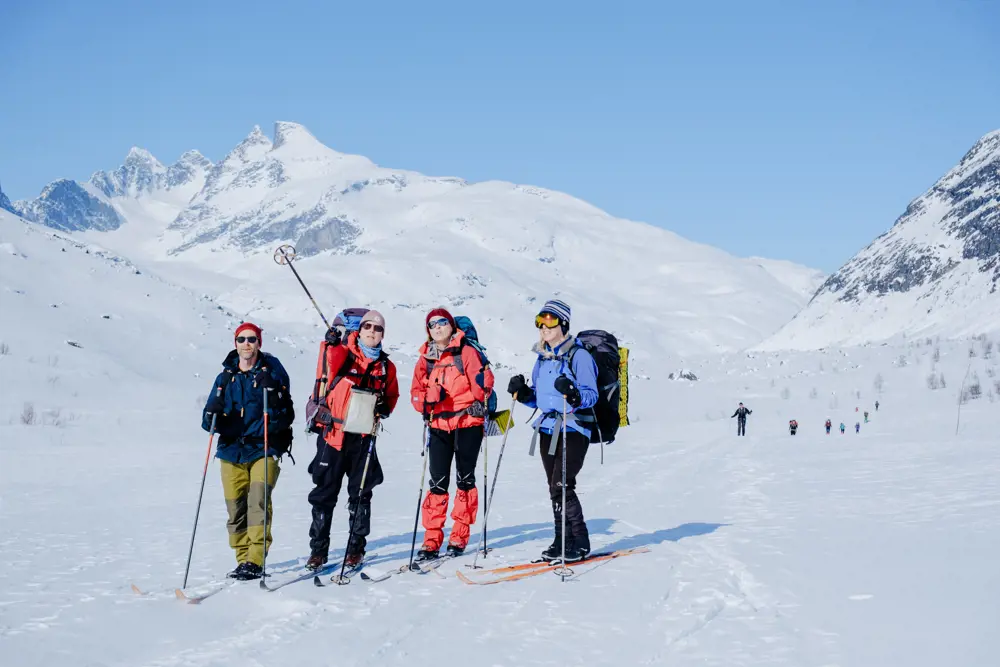 Gruppe på ski blant snøkledde fjell.