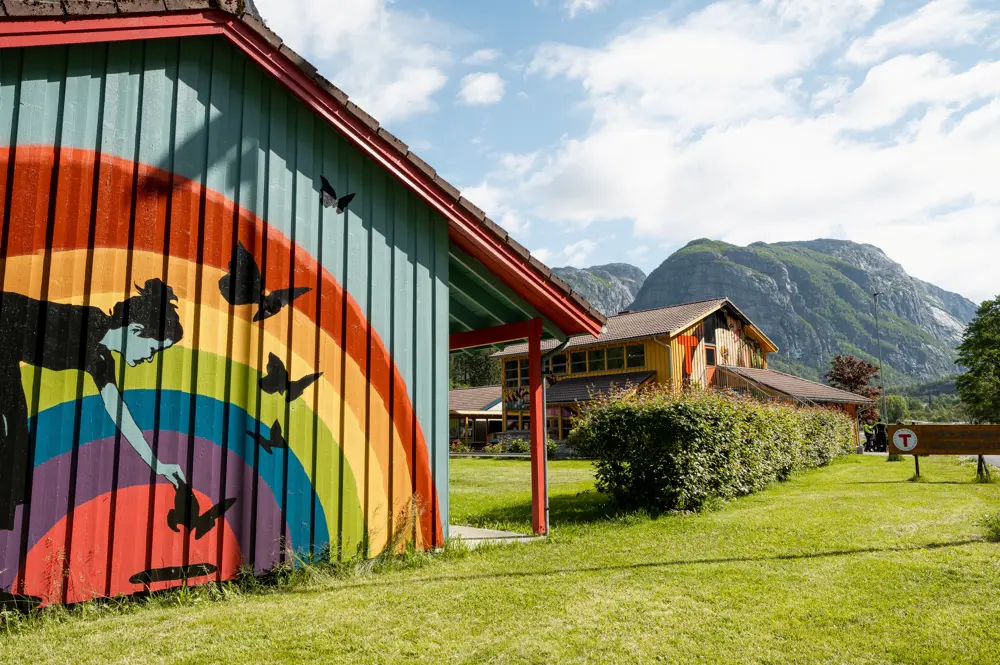 Et hytteanlegg som er malt i regnbuens farger. Her ser vi en vegg som det er malt en regnbue på med en rame som gir mat til fuglene.