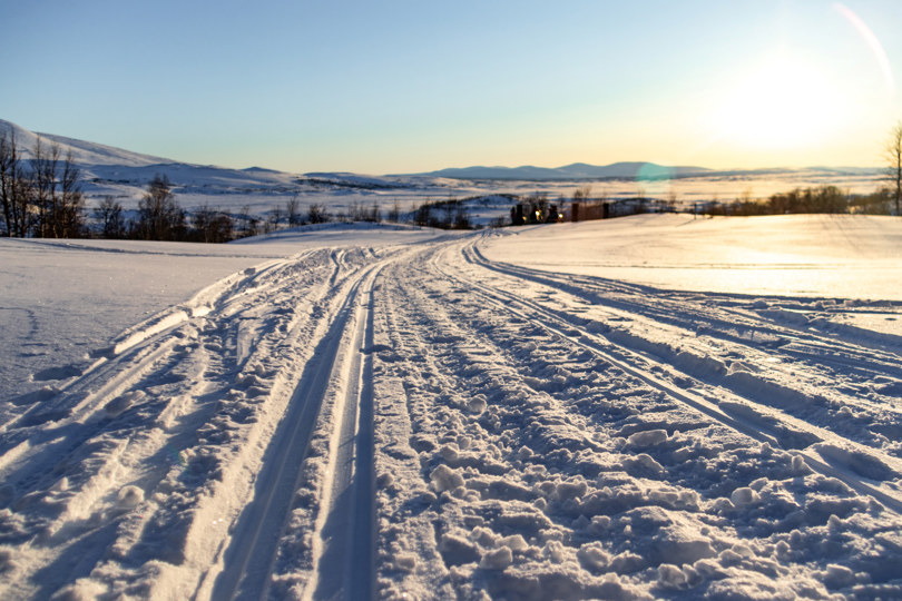 Et snødekket lanskap om vinteren, hvor oppkjørte skispor strekker seg fra synspunktet og innover i  bildet. Skyfri himmel. 