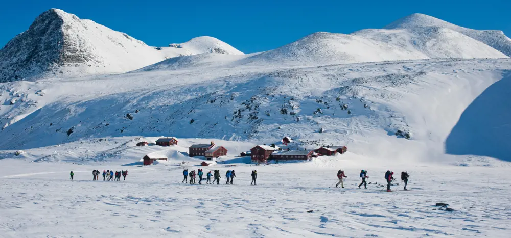 Fra de rødbrune hyttene på Rondvassbu går turfølge på ski inn i fjellheimen. 