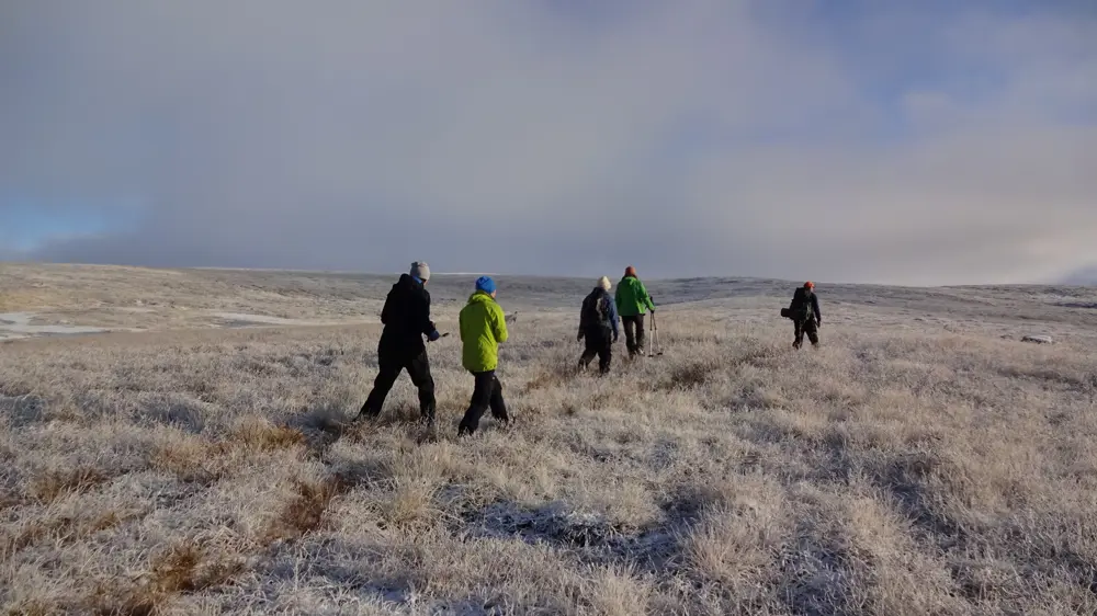 Fem voksne som går over rimfrosset landskap
