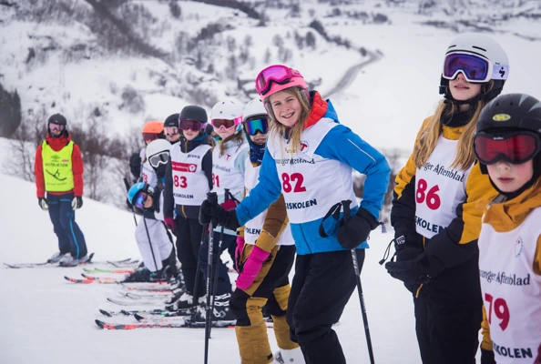 Deltakere på skiskolen ser inn i kamera, stående på rekke i skibakken