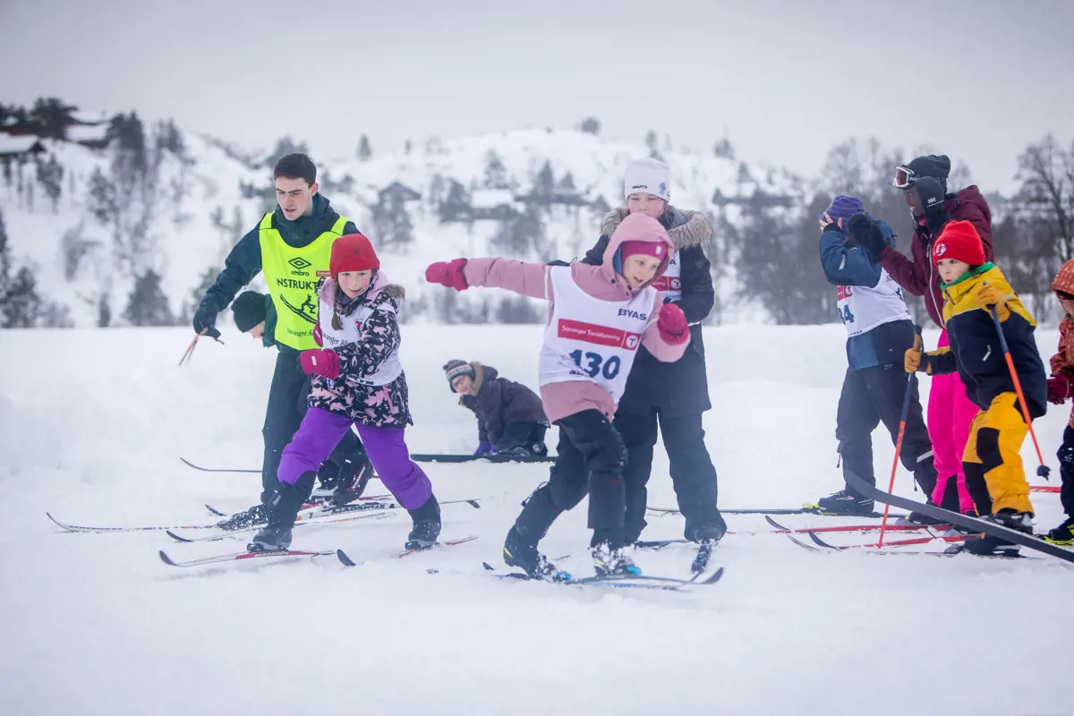 Barn med startnummer og langrennski går rundt på snøen