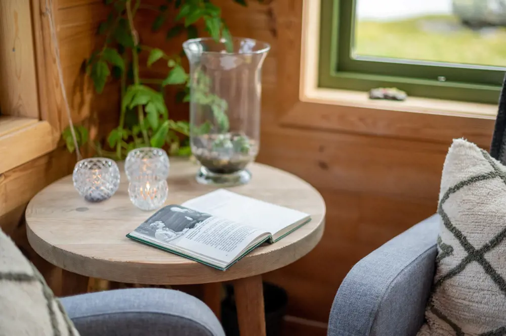 Nærbilde av en bok og en lyslykt som er plassert på et bord i stuen av hytta.