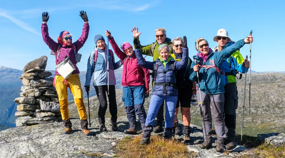 Gjeng glade turgåere med hendene i været på toppen av et fjell.