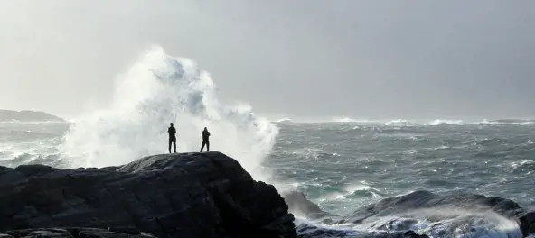 To mennesket står på svaberg og ser på store bølger ute i havgapet. Foto 