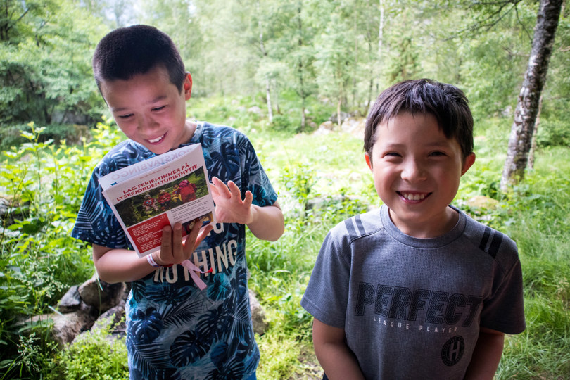 Barn som smiler ute på tur og leser i en brosjyre.