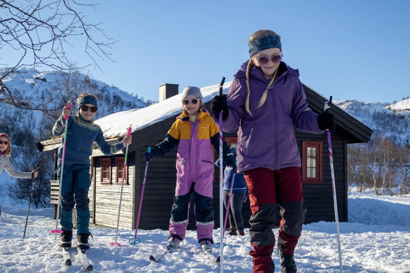 Tre jenter går på ski utenfor ei turisthytte.