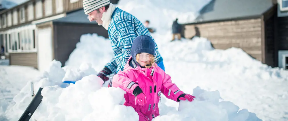 Far og datter som leker i snøen utenfor hytta. 