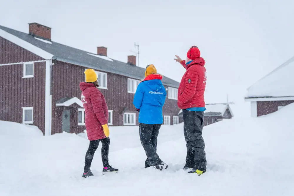Bilde av tre personer som står foran DNT hytta Glitterheim. Vinteren 2023.