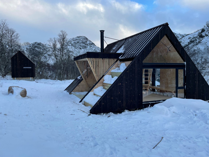 Snødekt landskap med en dagsturhytte og et tilbygg i brunt panel.