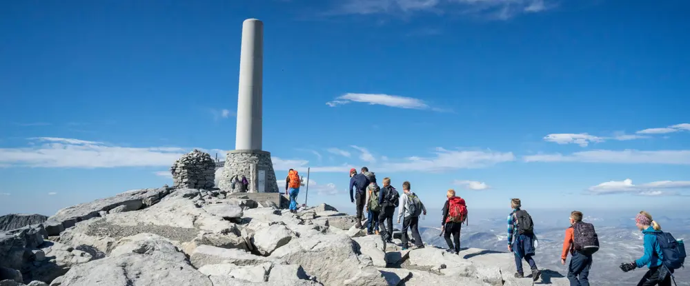 Svart hytta med røde detaljer, flagrende norsk flagg og åpent fjellandskap