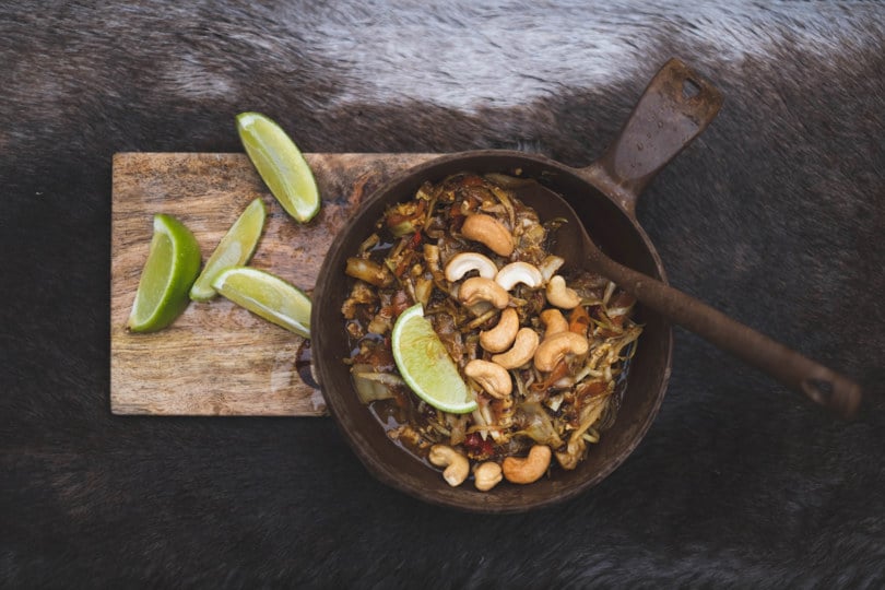 Nærbilde av stekte nudler med cashewnøtter og limebiter på toppen.