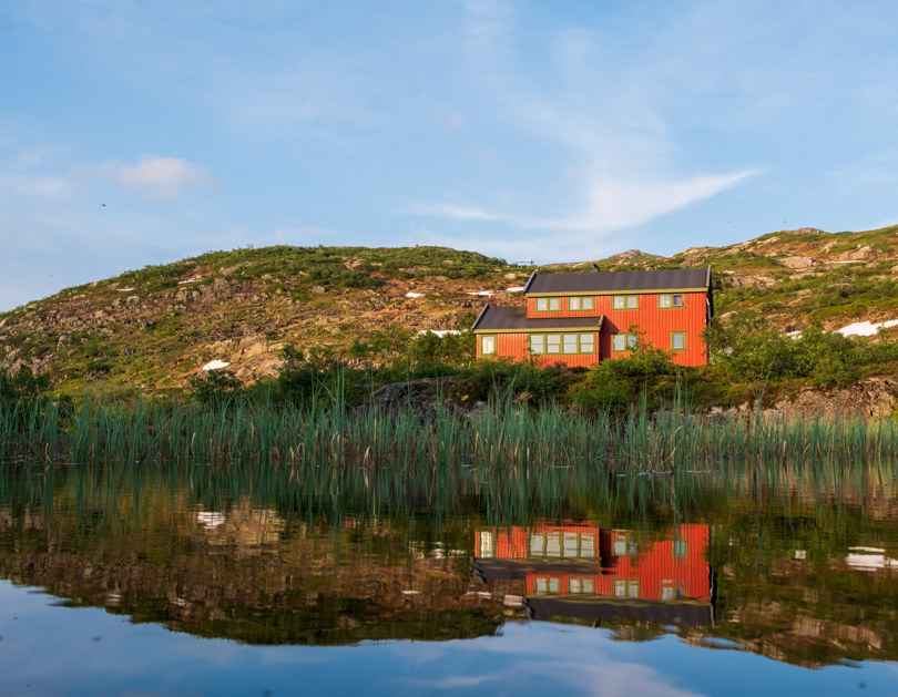 En rød hytte som speiler seg i vannet.