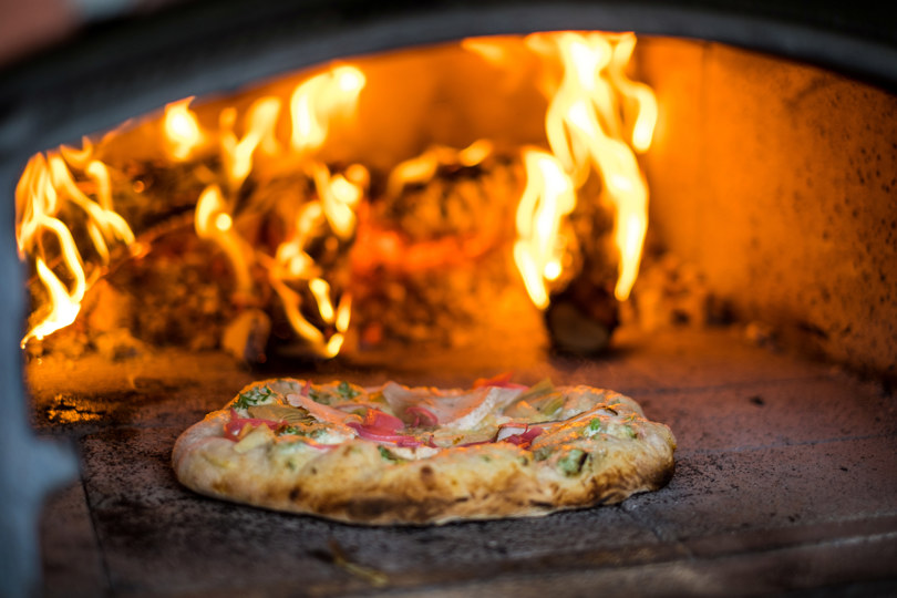Nærbilde av en pizza på vei inn i en vedfyrt pizzaovn.