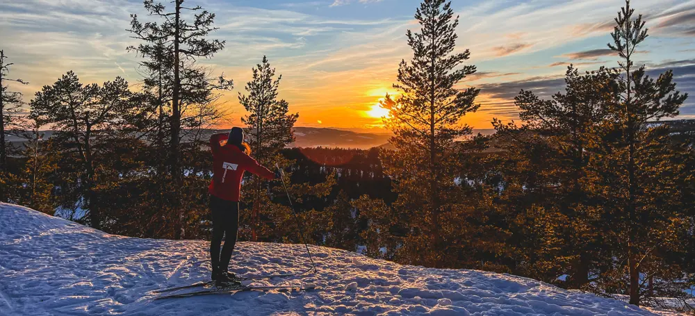 Menneske som står og ser utover mot solnedgang på ski