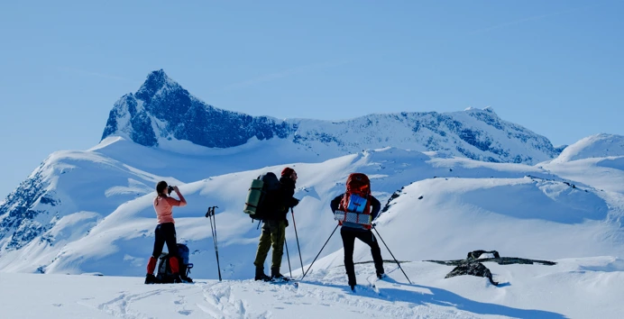 Tre personer med fjellski som nyter utsikten i vinterfjellet