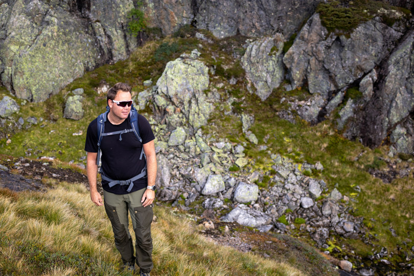 Mann med solbriller som står i et fjellterreng og smiler.