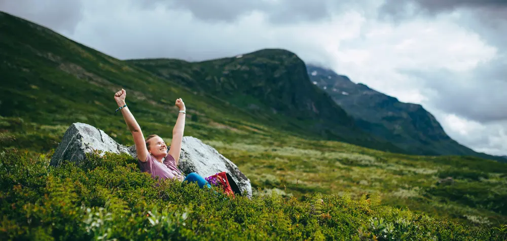 Dame sitter i fjellet og strekker armene i været. 