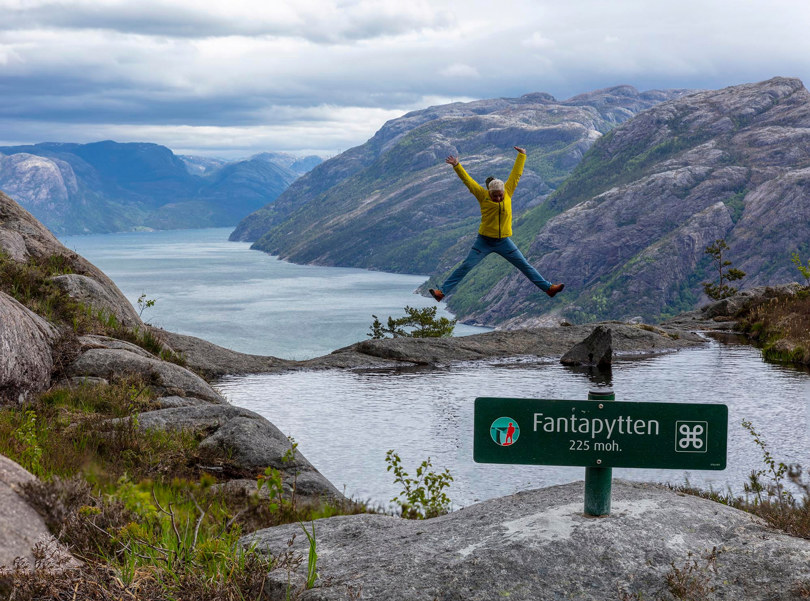Person som hopper ved en stor pytt med utsikt til Lysefjorden bak.