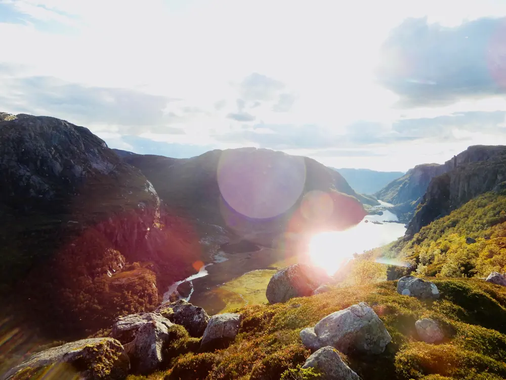 Solen som skinner mot steiner, gress, fjell og vann