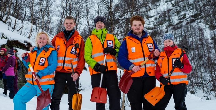 Fem personer med oransje vester og hver sin spade står i snøen og smiler