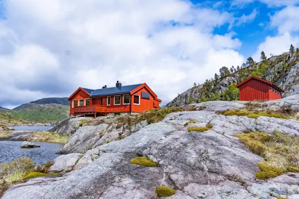 Rød hytte og rødt toalettbygg som ligger plassert på et svaberg.