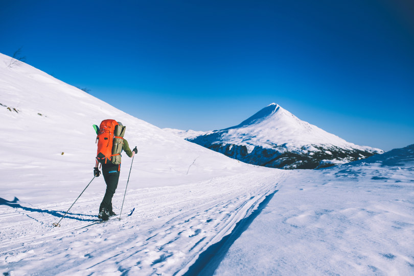 Skiløper med oransje sekk følger skuterspor innover i fjellet.